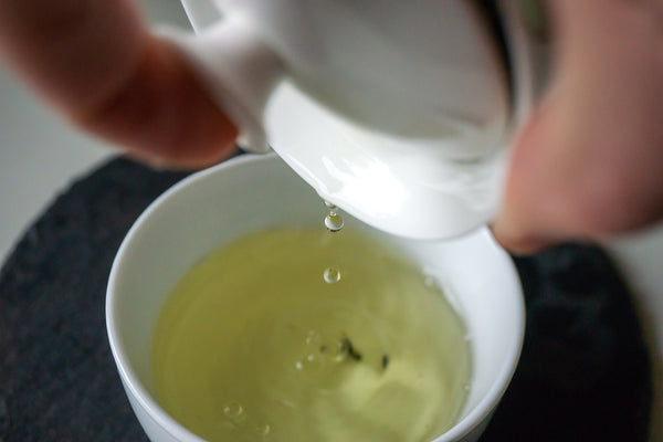 Heller und klarer Tee wird aus einer Porzellan-Teekanne in eine Tasse gegossen. 