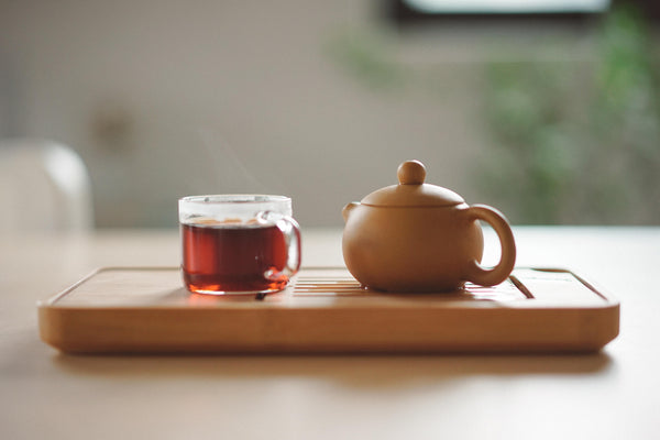 Ein terracottafarbenes Brett, auf dem eine Teekanne und eine Tasse mit rötlichem Tee stehen